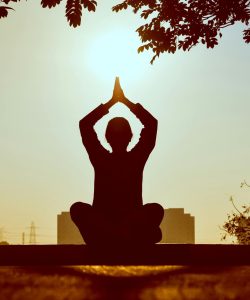 Silhouette of a person practicing yoga outdoors during sunrise, creating a calming atmosphere.
